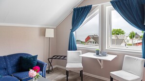 A room with a blue sofa, two white chairs, a small table with a vase of flowers, and a window with curtains. - Moens Motell (Vanylven)