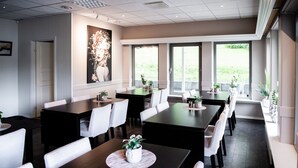 A modern dining area with multiple tables and chairs, large windows, and indoor plants. - Moens Motell (Vanylven)