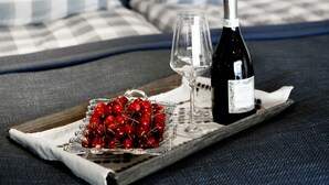 A bed with checkered bedding, a tray with a bottle and glasses, and a bowl of cherries. - Moens Motell (Vanylven)