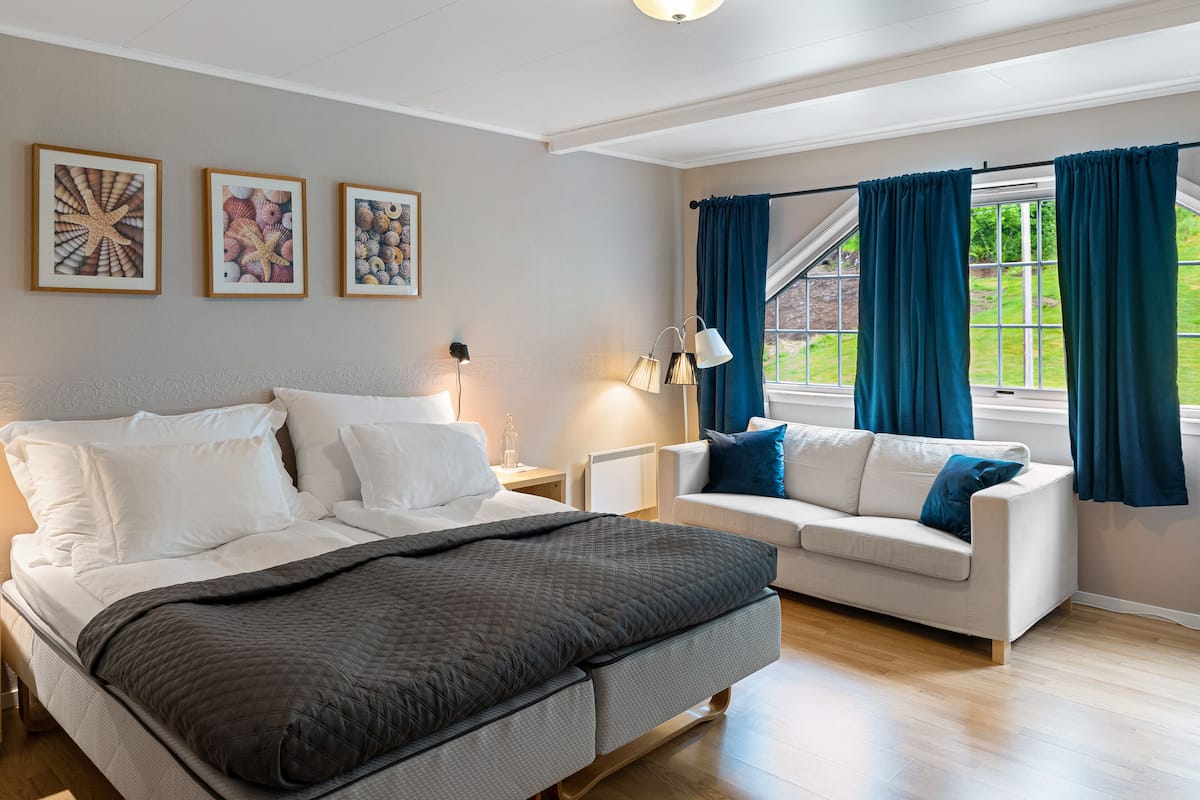 A bedroom with a bed, a sofa, a nightstand, and a window with curtains.