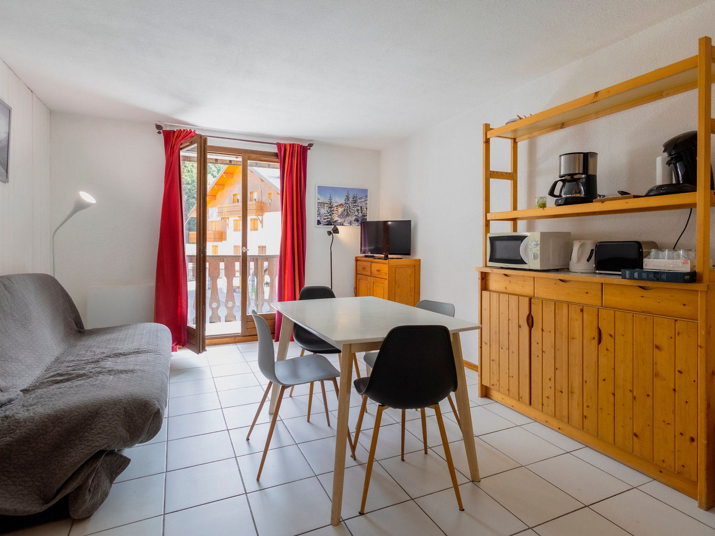 A room with a dining table, chairs, a sofa, a TV, and a kitchen area with a coffee maker and microwave.