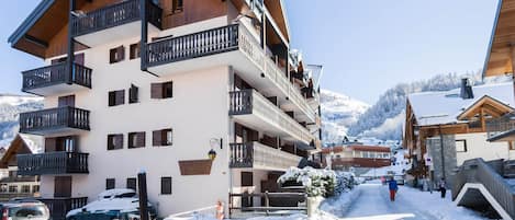 A multi-story hotel with balconies, a snow-covered street, and mountains in the background.