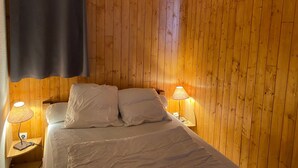 Et soveværelse med vægpaneler i træ, en seng med hvide sengetøj, to sengeborde med lamper, og en mørk gardin.