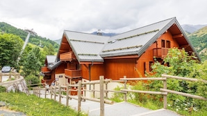A wooden lodge with a sloped roof, a wooden fence, and a mountainous backdrop.