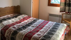 A bedroom with a bed, a wooden headboard, a window with a view of greenery, and a radiator.