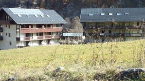 Un bâtiment doté de nombreux balcons et d’un toit plat, entouré d’un champ verdoyant et bordé de montagnes en arrière-plan.
