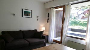 Une pièce avec un canapé marron foncé, une table en bois, une lampe et une vue sur une maison, visible à travers une porte coulissante.