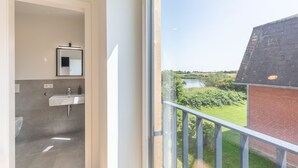 Ein modernes Badezimmer mit Waschbecken und Spiegel, ein Balkon mit Blick auf einen Garten und ein Gebäude.