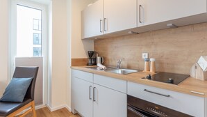 Eine moderne Küche mit weißen Schränken, einer Holzarbeitsplatte, einem eingebauten Ofen und einem Fenster mit Jalousien.