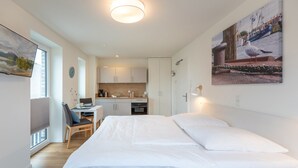 Ein modernes Schlafzimmer mit einem großen Bett, einem Schreibtisch mit Stuhl, einer Küchenzeile und einem Essbereich.