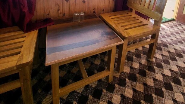 Un banco y una mesa de madera junto a una ventana con vista a la playa y las montañas.