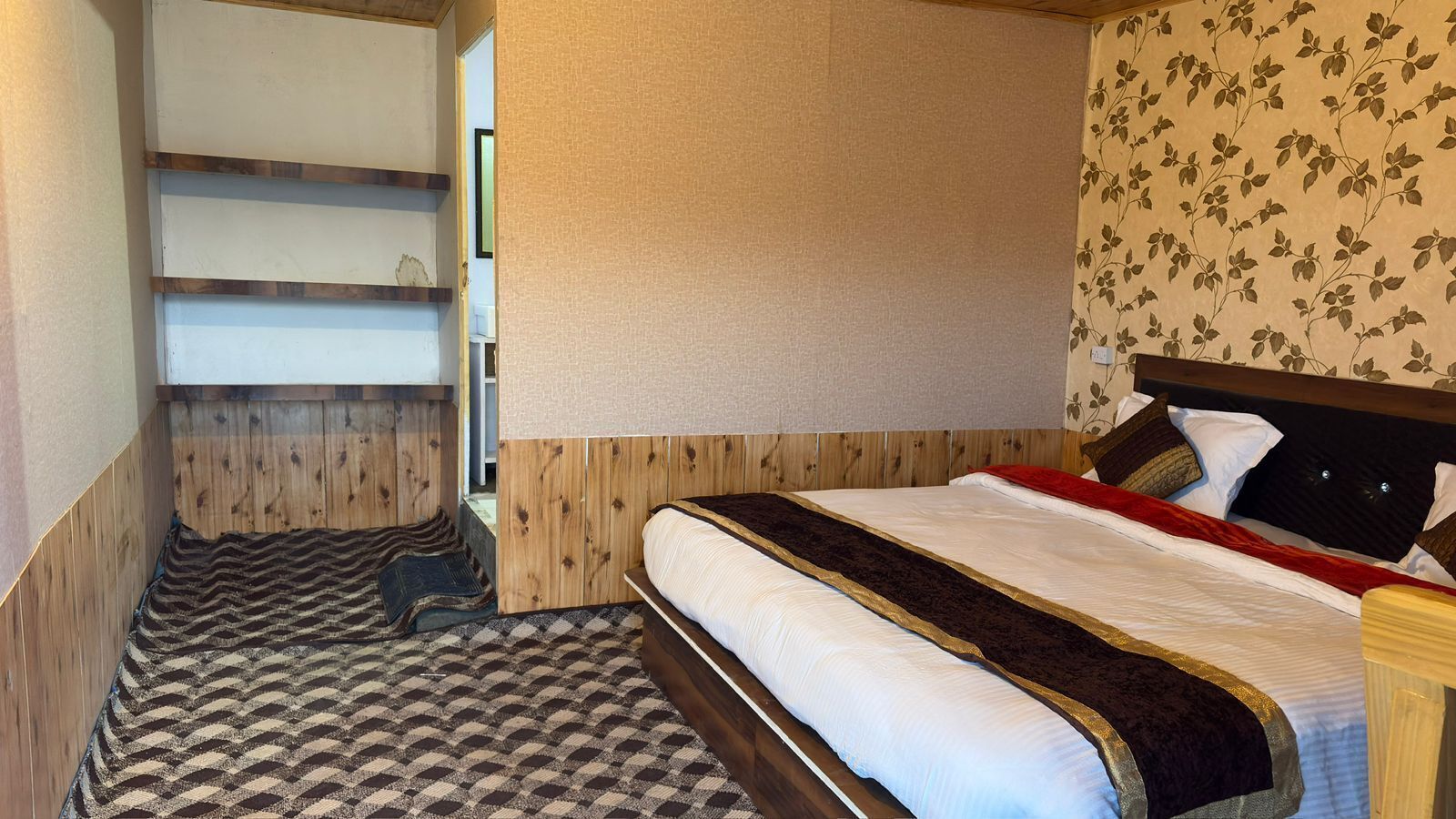 Quarto com cama, cabeceira de madeira, tapete estampado e parede com desenho floral.