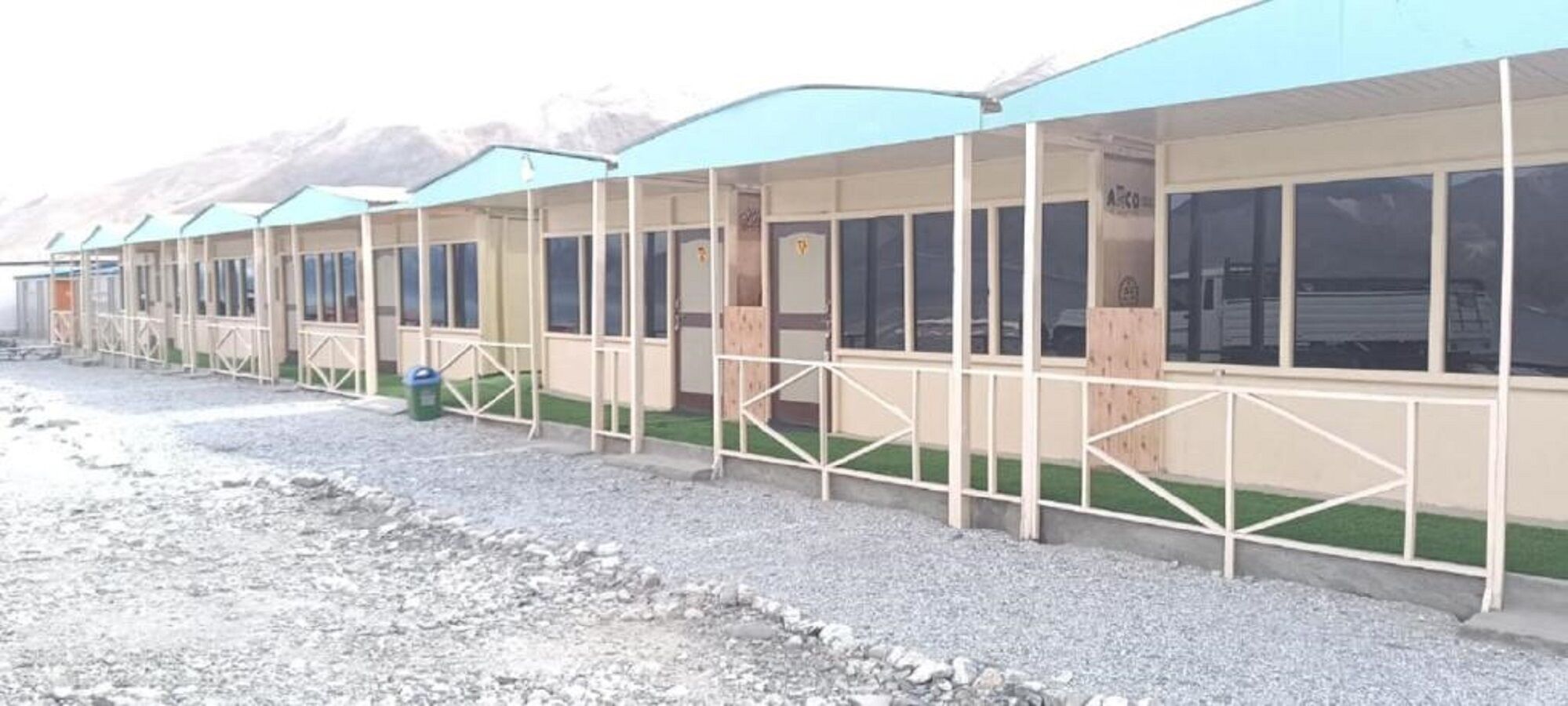 A row of single-story buildings with a simple, functional design, featuring large windows and a flat roof.
