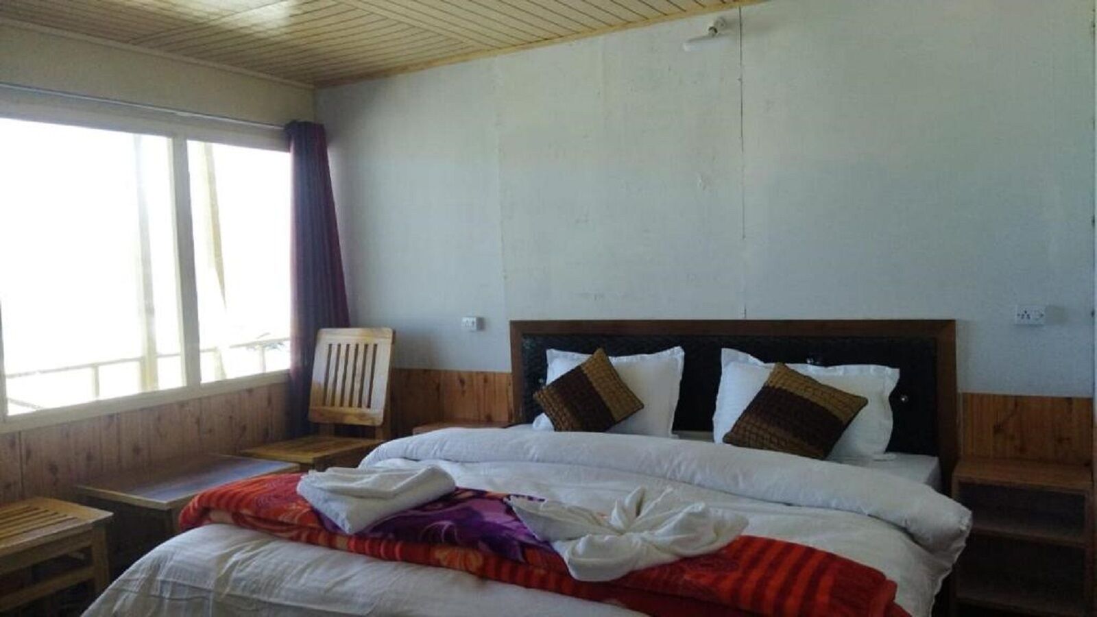 Ein Hotelzimmer mit einem hölzernen Kopfende, einem großen Bett mit weißer Bettwäsche, einem Nachttisch aus Holz und einem Fenster mit Vorhängen.