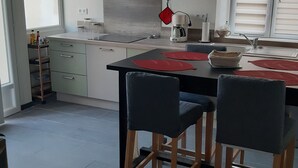 A modern kitchen with a black dining table, two chairs, a coffee maker, and a red hanging pot.