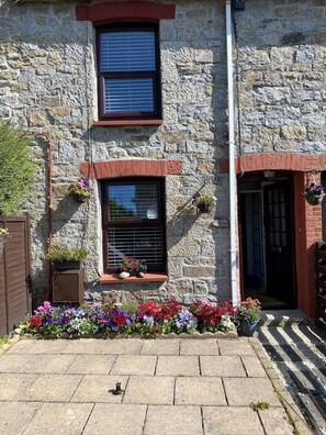 A stone building with a small window and a door, surrounded by a flower bed. - A beautiful 3 bedroom Cornish Cottage & wood stove (Falmouth)