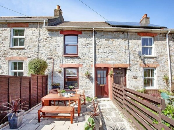 A stone house with a patio, wooden furniture, and a fenced garden. - A beautiful 3 bedroom Cornish Cottage & wood stove (Falmouth)