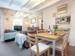 A cozy living room with a sofa, a dining table with chairs, and a TV in the background. - A beautiful 3 bedroom Cornish Cottage & wood stove (Falmouth)