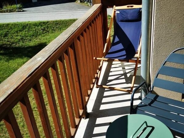 Um deck de madeira com uma cadeira dobrável azul e uma cadeira verde.
