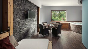 Una habitación moderna con pared de piedra, una cama, zona de comedor con sillas, un armario de madera y una bañera de hidromasaje.