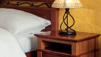 A wooden nightstand with a lamp, a drawer, and a bed with white linens.