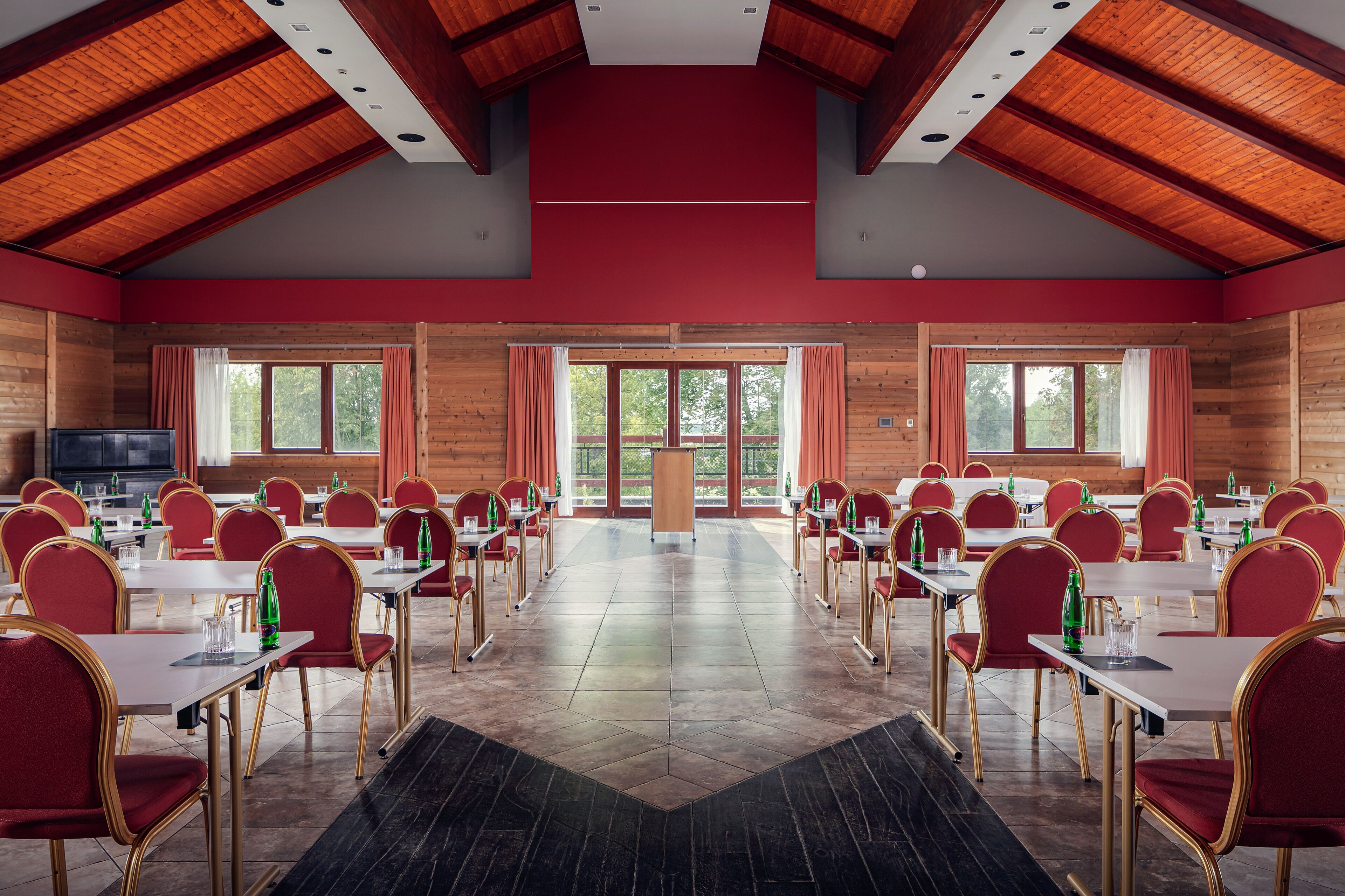 A conference room with multiple tables and chairs, wooden walls, and large windows.