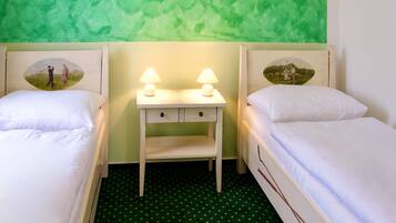 Quarto com duas camas, uma mesinha de cabeceira e luminárias, e um tapete verde estampado.