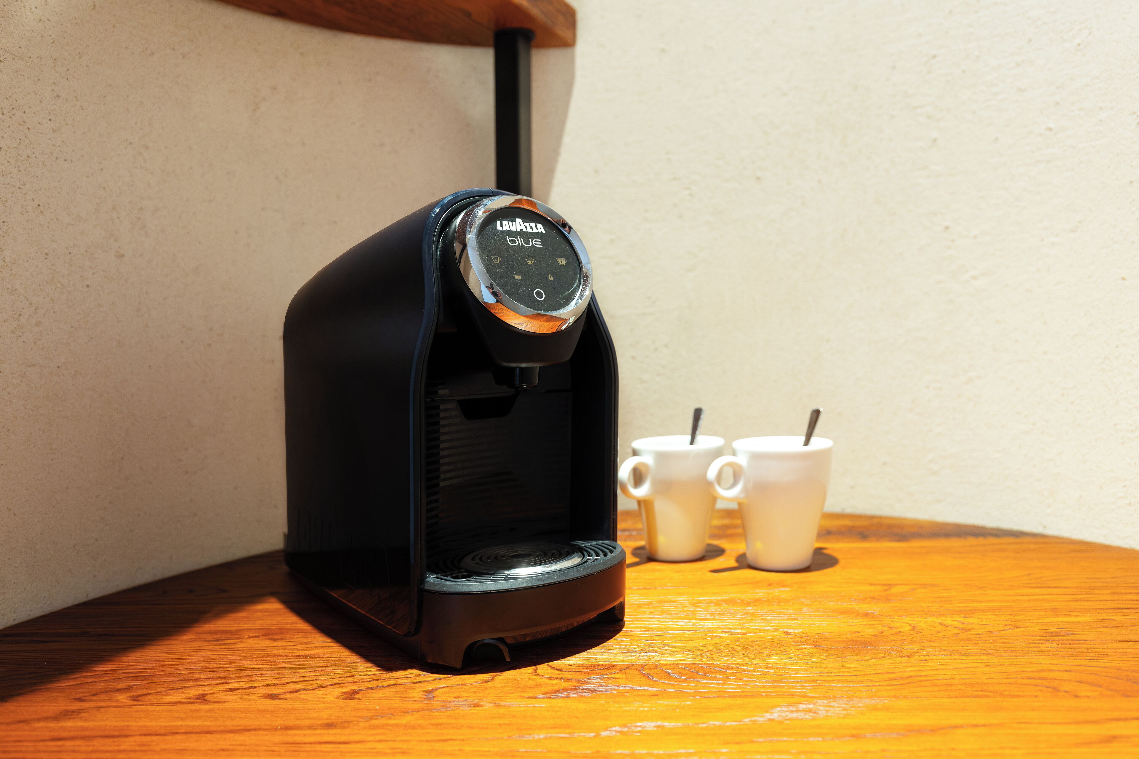 A coffee maker with a control panel, two white cups, and a wooden table.
