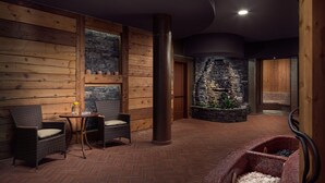 Un área de spa con paredes de madera, una pared de piedra, una bañera de hidromasaje y mobiliario de mimbre.