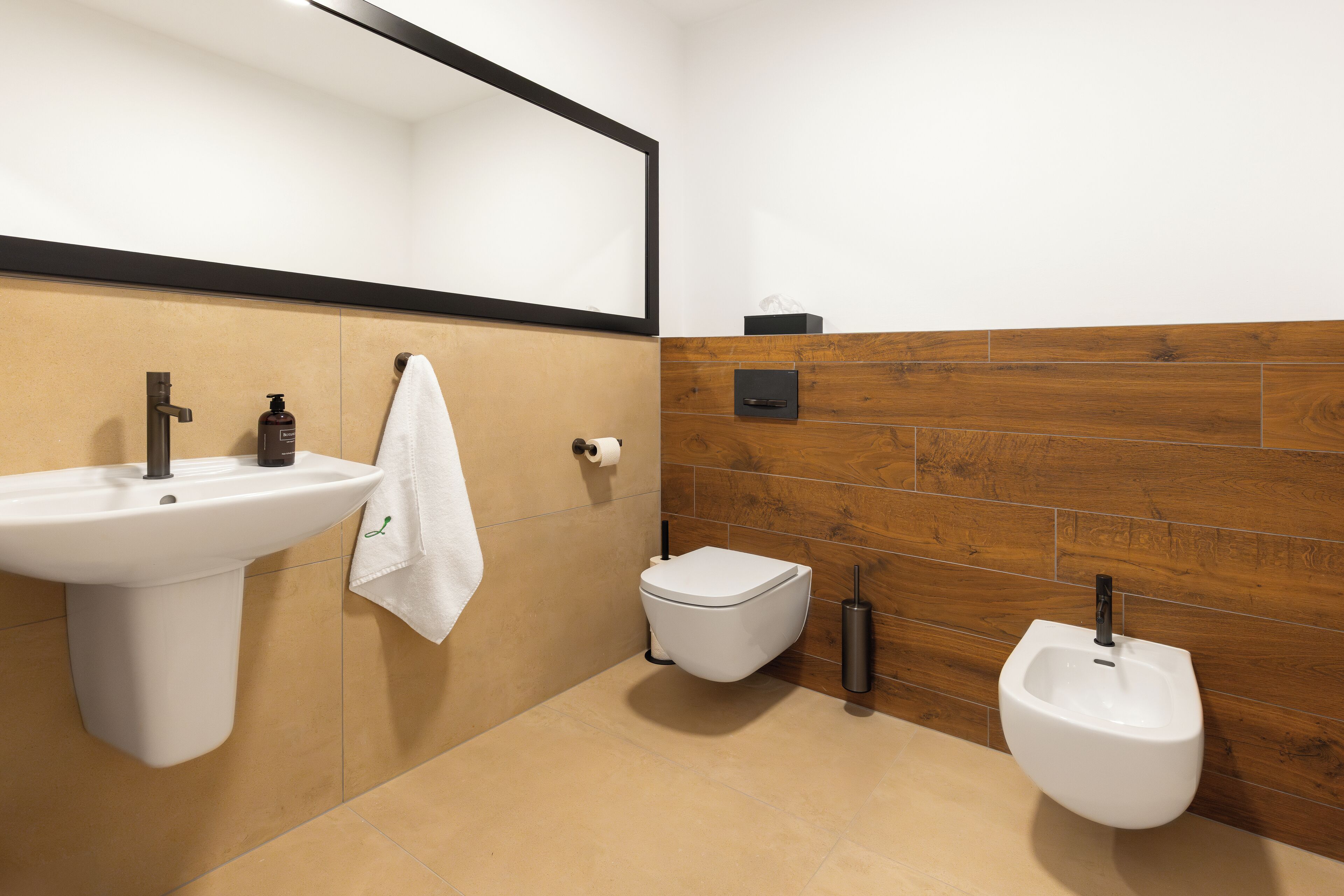 A modern bathroom with a pedestal sink, toilet, bidet, and a mirror above the sink.
