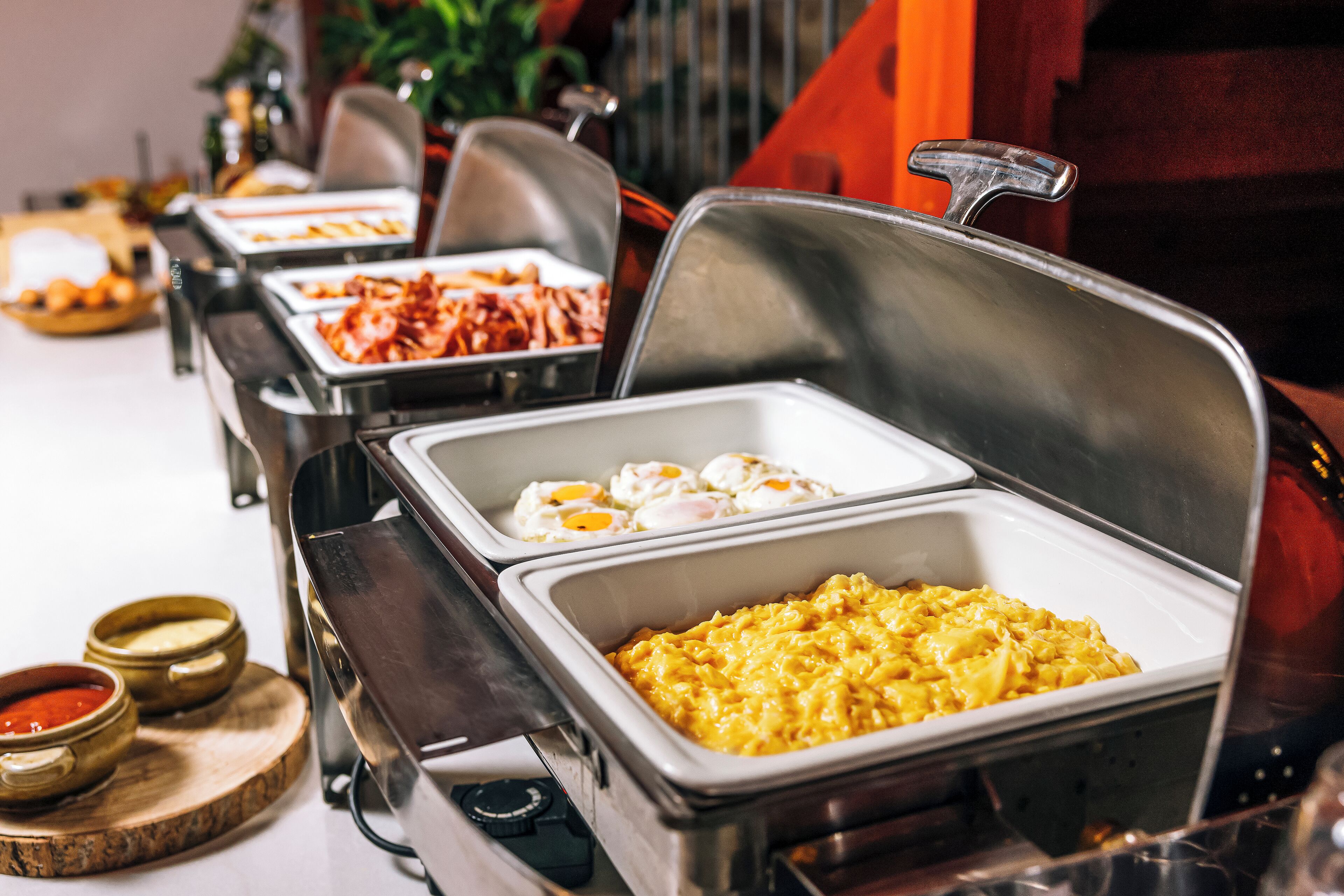 Un bufé con diversas opciones de comida, incluyendo huevos, macarrones y salsas.
