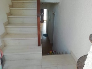 Una escalera conduce a una puerta con un pequeño ventanal. Hay algunos objetos en el suelo cerca de la puerta.
