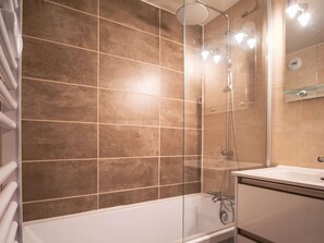 Een moderne badkamer met een douchecabine van glas, een witte badkuip en een wastafel met spiegel.