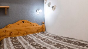 Een slaapkamer met een houten hoofdbord, een bed met een patroonspreidekking, een blauwe wand en een houten plank.
