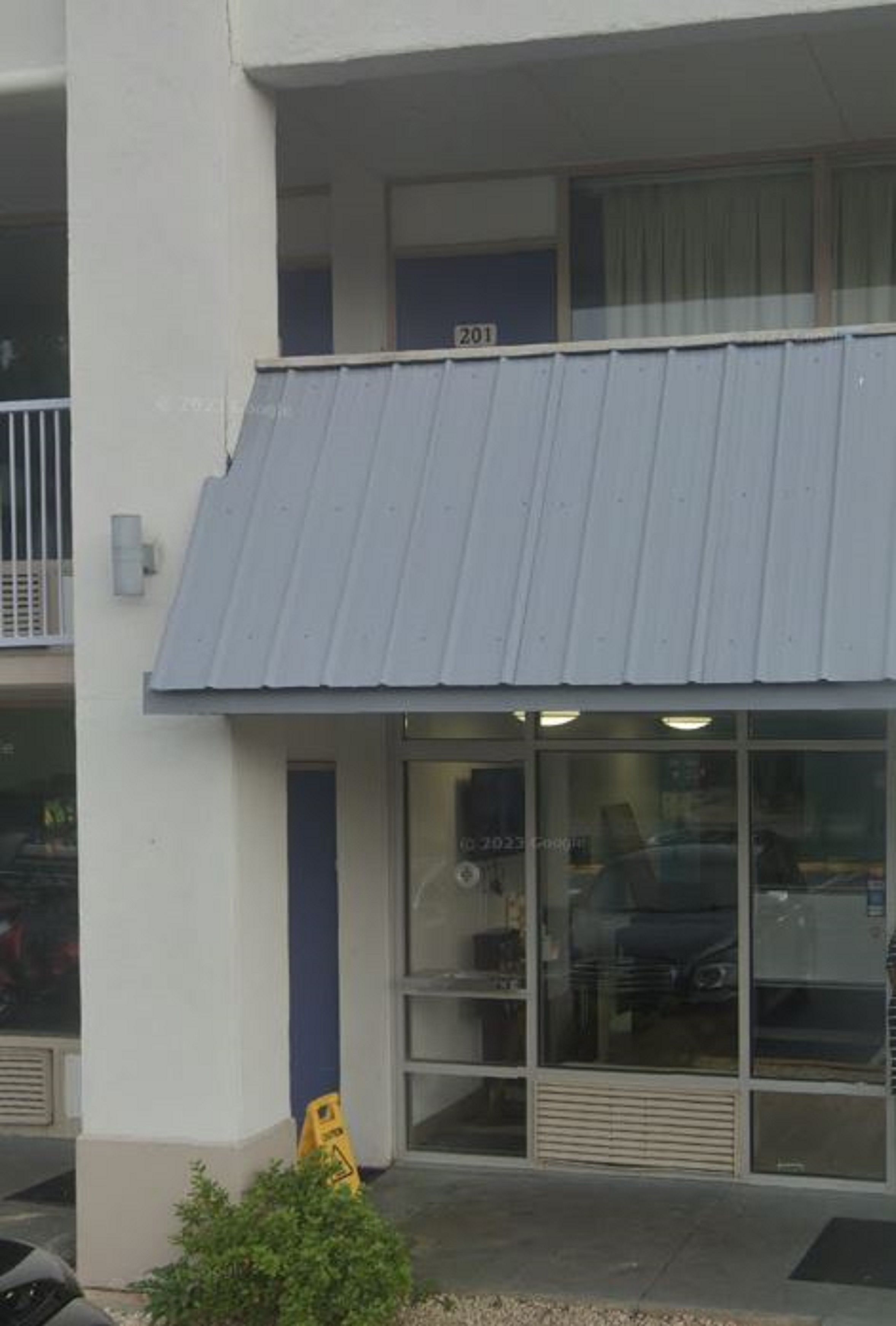 Un edificio con toldo azul, una puerta a la vista y una ventana con reflejo.