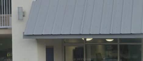 Un bâtiment doté d’un auvent bleu, d’une porte bien visible et d’une fenêtre dont la surface réfléchit la lumière.