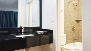 Un baño con un lavamanos negro, un espejo, una ducha con pared color beige y un inodoro blanco.