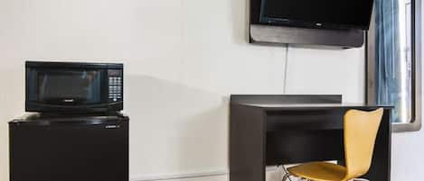 A compact kitchenette with a microwave, a small refrigerator, a flat-screen TV mounted on the wall, and a modern chair.