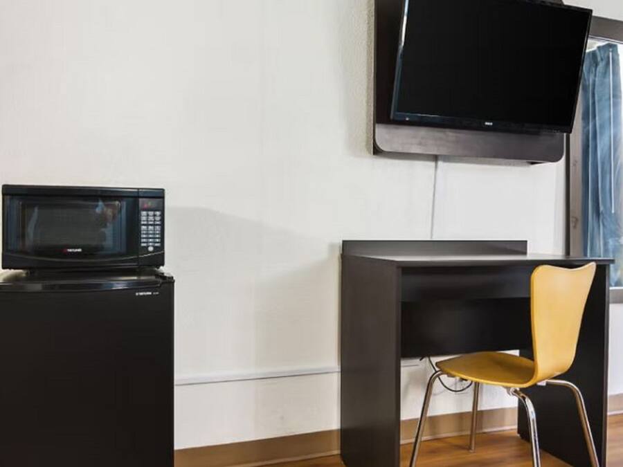 Een compacte kitchenette met een magnetron, een kleine koelkast, een flatscreen televisie aan de wand en een moderne stoel.