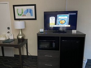 Een hotelkamer met een televisie, een lamp, een magnetron en een kunstwerk in een lijst aan de muur.