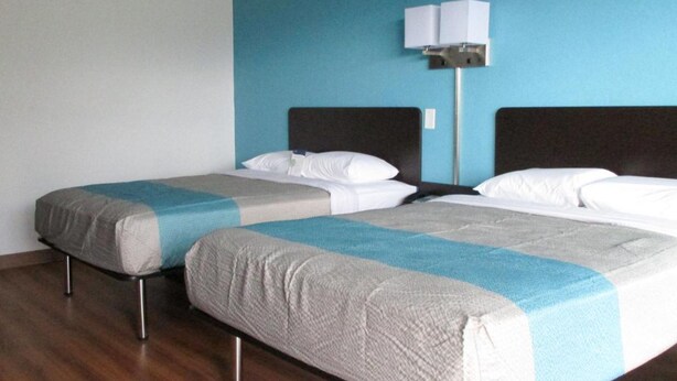 Dos camas individuales con ropa de cama gris y azul, suelo de madera y una lámpara fijada a la pared.