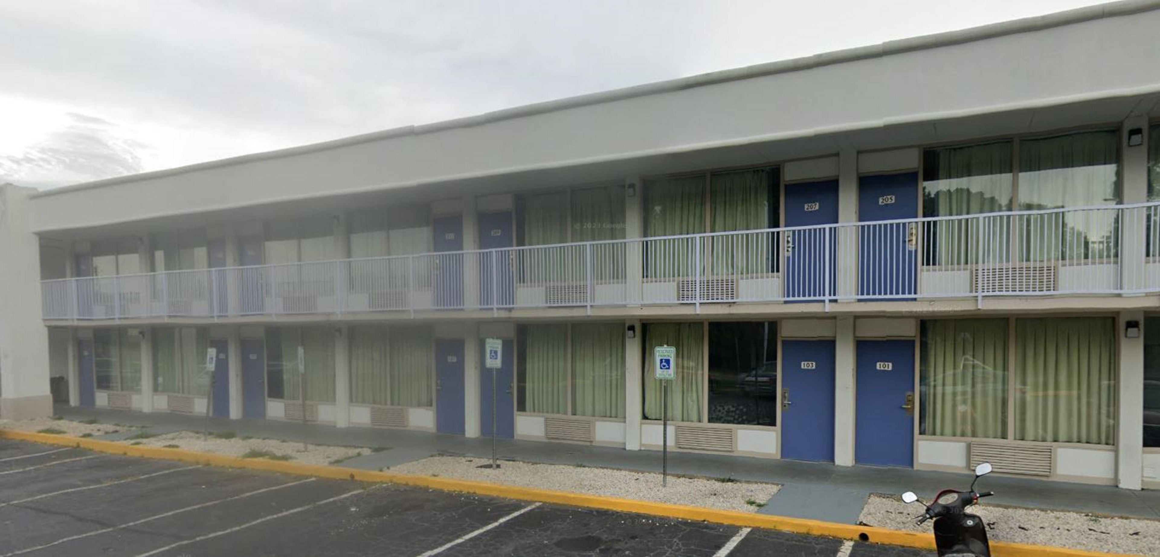 Un motel con aparcamiento y una moto estacionada al frente.