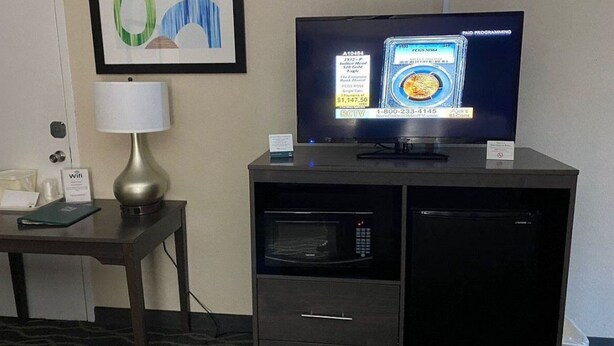 A hotel room with a TV, a lamp, a microwave, and a framed artwork on the wall. - Rodeway Inn Asheboro (Asheboro)