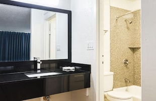 Un baño con un lavamanos negro, un espejo, una ducha con pared color beige y un inodoro blanco.