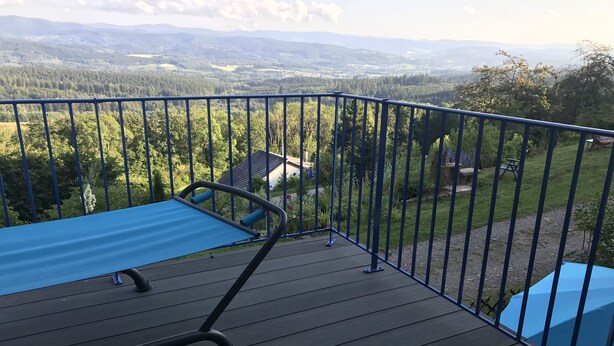 A deck with a blue mat and metal railing overlooking a forested valley.