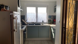 A compact kitchen with a refrigerator, stove, sink, and a window with curtains.