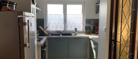 A compact kitchen with a refrigerator, stove, sink, and a window with curtains.