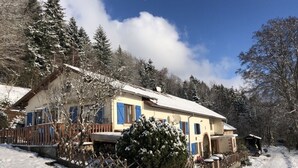 A snow-covered house with a wooden fence, a snow-covered tree, and a clear sky.