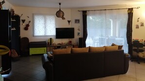 Un salón con sofá, televisión y ventana con cortinas.