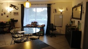 Un comedor con una mesa redonda, sillas y una araña. Se observa una ventana con cortinas, una pizarra y adornos en la pared.